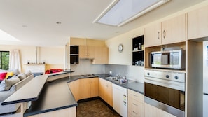 Cocina compacta con microondas, horno y lavavajillas integrados. Cuenta con una zona de estar con sofá y una mesa de comedor.