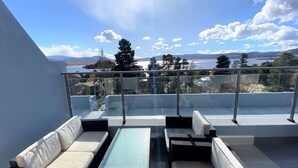 Un balcon doté d’une balustrade en verre, d’un espace salon extérieur et offrant une vue sur un lac et des montagnes.