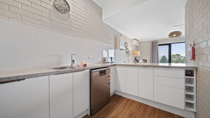 Une cuisine moderne avec des meubles blancs, un lave-vaisselle en acier inoxydable et un mur de fond en briques apparentes.