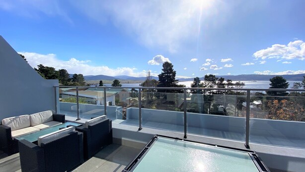Une terrasse sur le toit dotée d’une balustrade en verre, d’un espace salon extérieur et offrant une vue sur un lac et des montagnes.