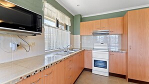 A kitchen with wooden cabinets, a built-in oven, a microwave, and a sink.