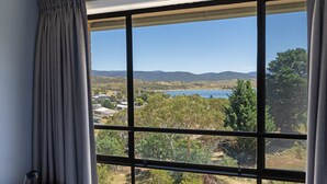 A room with a large window offering a view of a lake, hills, and a residential area.