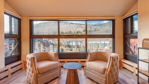 Una habitación con dos sillones, una mesa redonda y grandes ventanales que ofrecen vistas a un paisaje montañoso.