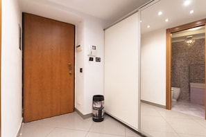 Een gang met een houten deur, een afvalbak en een schuifdeur naar een badkamer.