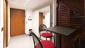 Ein Zimmer mit Holztür, Tisch mit Stühlen, Spiegel und einer Treppe.