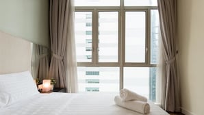 A hotel room with a large window, a neatly made bed, a bedside lamp, and a rolled towel on the bed. - Elysees Suite Marc Residence KLCC (Kuala Lumpur)