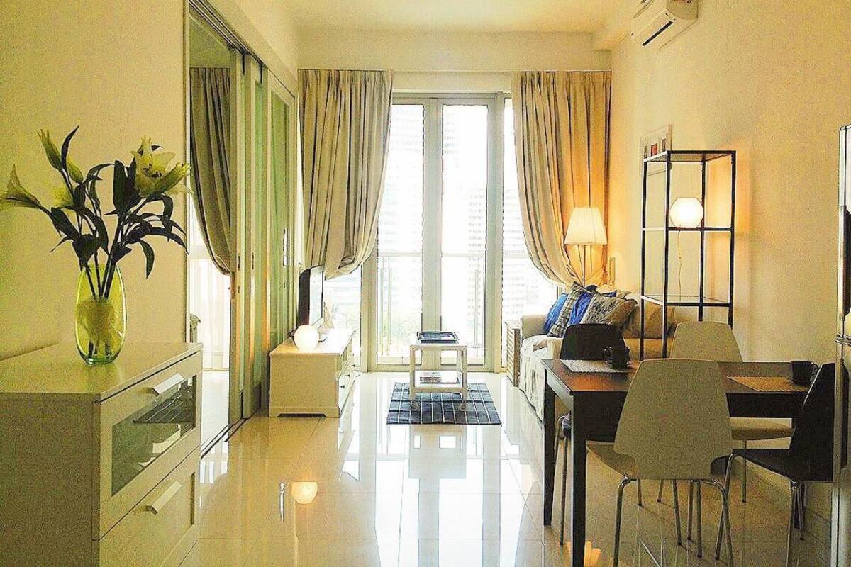 Une chambre d’hôtel avec un coin repas, une petite table avec des chaises, une lampe et une vue sur la ville grâce à de grandes fenêtres.