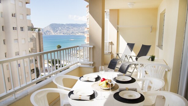 Ein Balkon mit Esstisch für zwei Personen, weißen Plastikstühlen und Blick auf das Meer und die Gebäude.