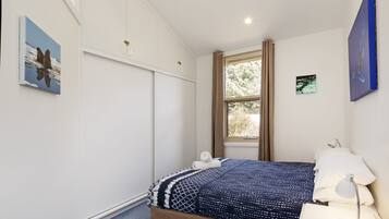 Een slaapkamer met een bed, een raam en een schilderij aan de muur.
