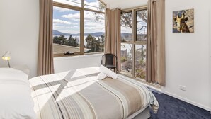 Une chambre à coucher avec un lit, une chaise, une fenêtre avec des rideaux et un tableau accroché au mur.