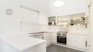 Une cuisine moderne avec des meubles blancs, un four à micro-ondes encastré, une cuisinière et un évier.