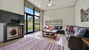 A modern living room with a fireplace, large windows, a sofa, and a coffee table. - Ecocrackenback Luxe Chalet 19 (CRACKENBACK)
