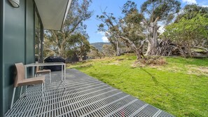 A modern outdoor seating area with a metal table and chairs, overlooking a grassy landscape with trees and a clear sky. - Ecocrackenback Luxe Chalet 19 (CRACKENBACK)