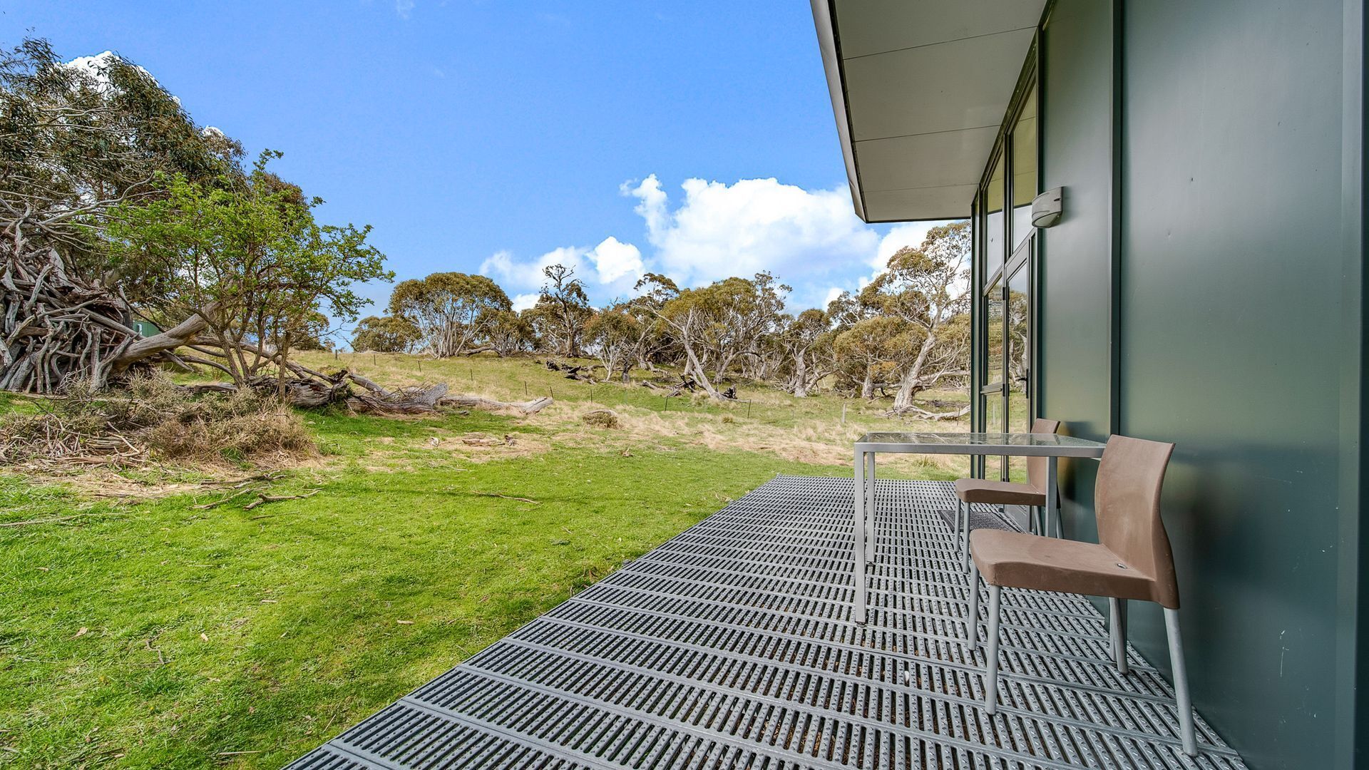 A balcony with a metal grid floor, overlooking a grassy area with trees and a hill in the background.