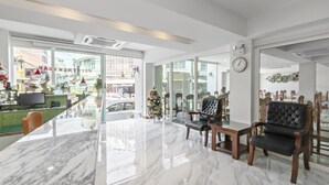 A modern hotel lobby with a marble reception desk, leather armchairs, and a large window offering a view of the street. - Royale 8 Ville (Bangkok)