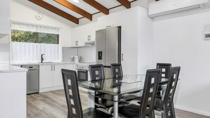 Une cuisine moderne avec des meubles blancs, un réfrigérateur en acier inoxydable et une table à manger en verre, assortie de chaises noires.