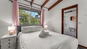 Un lit bien fait, avec du linge de lit blanc, une table de chevet avec une lampe et une fenêtre ornée de rideaux roses.