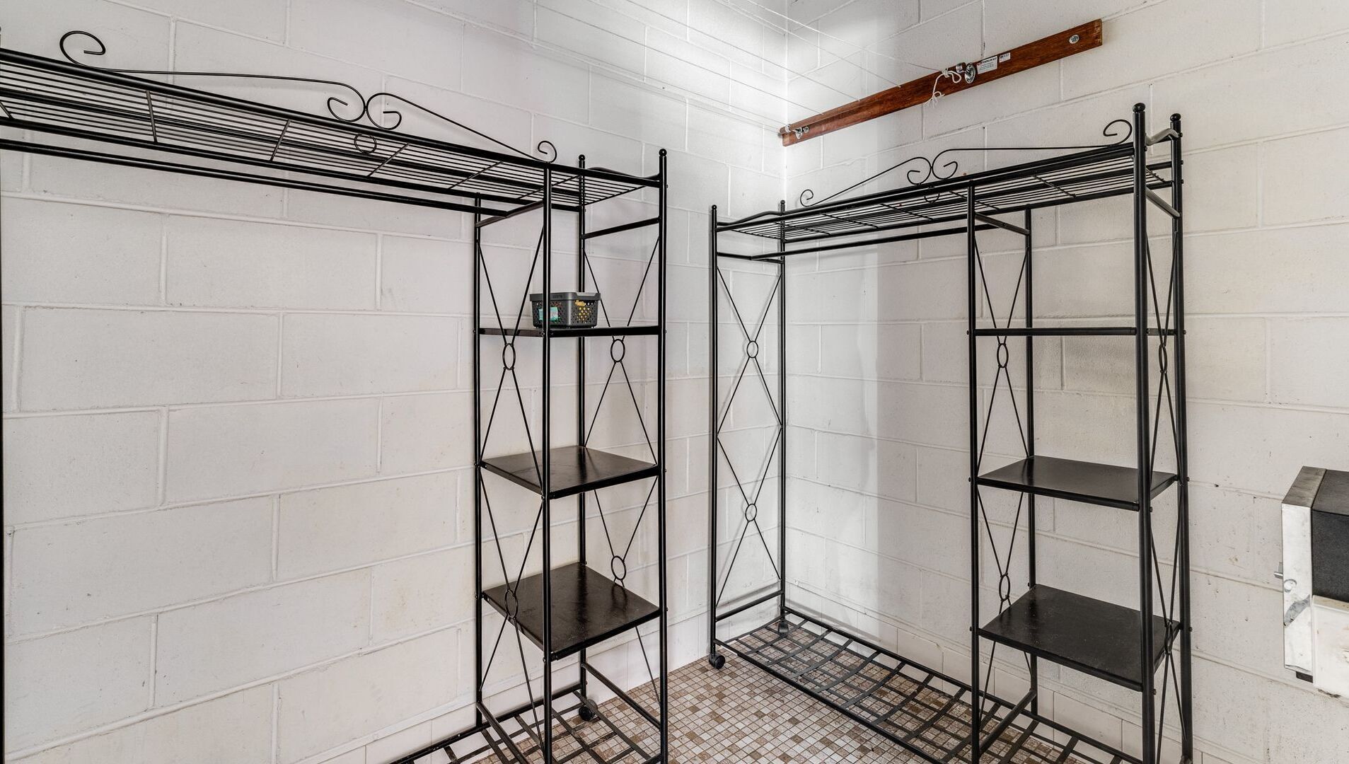 A corner with two black metal shelving units against a white brick wall, with a small wooden shelf above one unit.