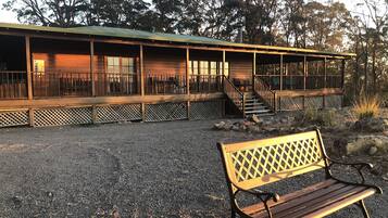 A wooden cabin with a balcony, a gravel driveway, and a bench.