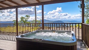 A hot tub under a wooden pergola with a view of mountains and a lake.
