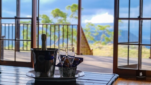 A table with a bucket, glasses, and a bottle, with a scenic view through large windows.