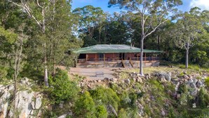 A rustic lodge with a green roof, surrounded by dense trees and rocky terrain.
