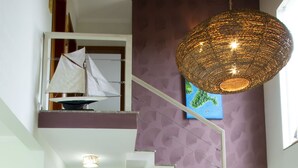 Un salón amplio con techo alto, una mesa de comedor con sillas, un sofá de mimbre y una escalera.