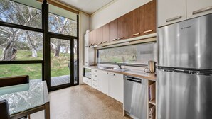 Una cocina moderna con refrigerador de acero inoxidable, armarios de madera y un amplio ventanal con vistas a un jardín.
