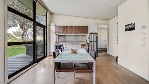 Una cocina moderna con armarios blancos, un refrigerador de acero inoxidable y un comedor con mesa de vidrio y sillas de cuero.