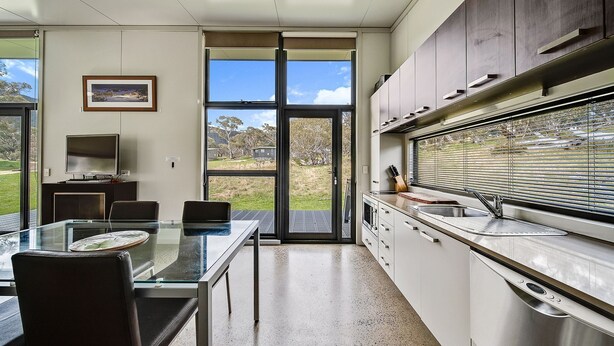 A modern kitchen with a glass dining table, stainless steel appliances, and a view of the outdoors. - Ecocrackenback 16 'Sustainable chalet close to the slopes.' (CRACKENBACK)