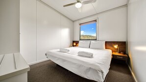 A hotel room with a large bed, a nightstand, a window with a view of the outdoors, and a ceiling fan. - Ecocrackenback 16 'Sustainable chalet close to the slopes.' (CRACKENBACK)