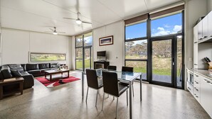 A modern living room with a glass dining table, black leather sofa, and a red rug. - Ecocrackenback 16 'Sustainable chalet close to the slopes.' (CRACKENBACK)