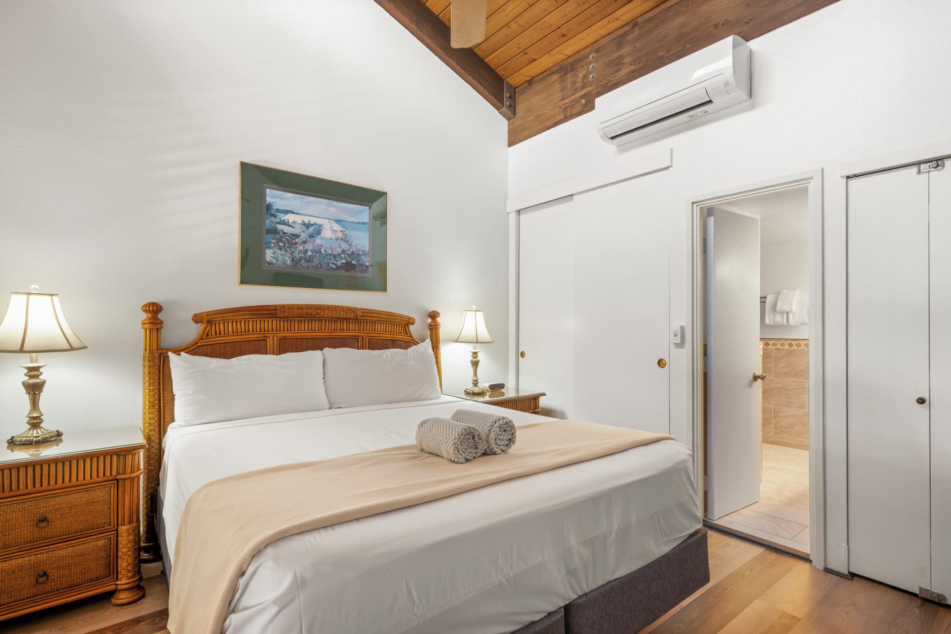 Ein Hotelzimmer mit einem Bett, Nachttischlampen, einem gerahmten Bild, einer Klimaanlage und einer Tür zu einem Badezimmer.