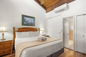 A hotel room with a bed, bedside lamps, a framed picture, an air conditioning unit, and a door leading to a bathroom.