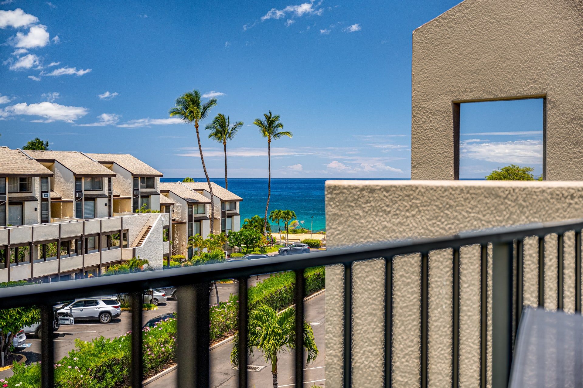 A beachfront hotel with multiple-story buildings, a parking area, and a view of the ocean.