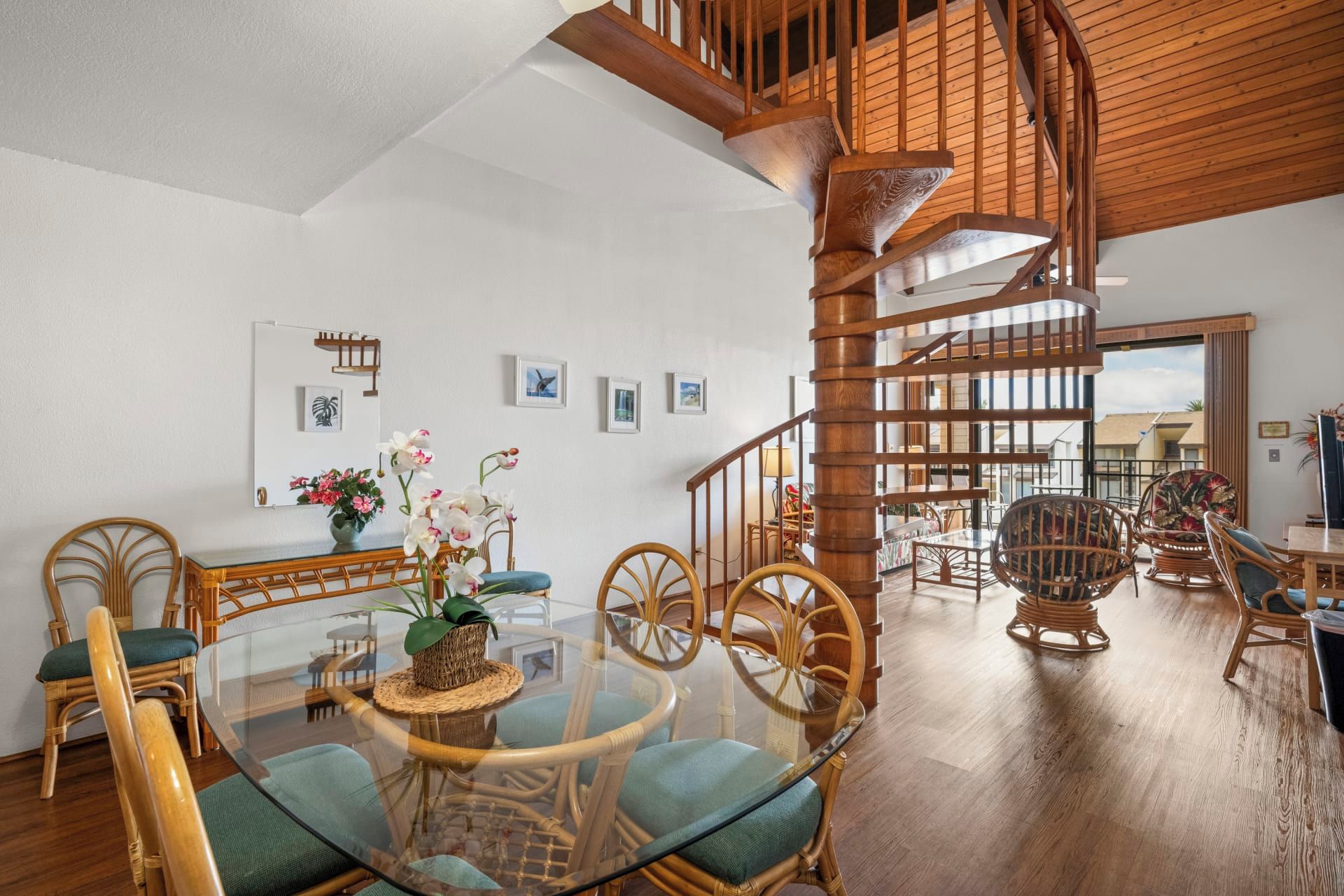 Um quarto espaçoso com escada em espiral de madeira, móveis de vime e mesa de jantar de vidro.