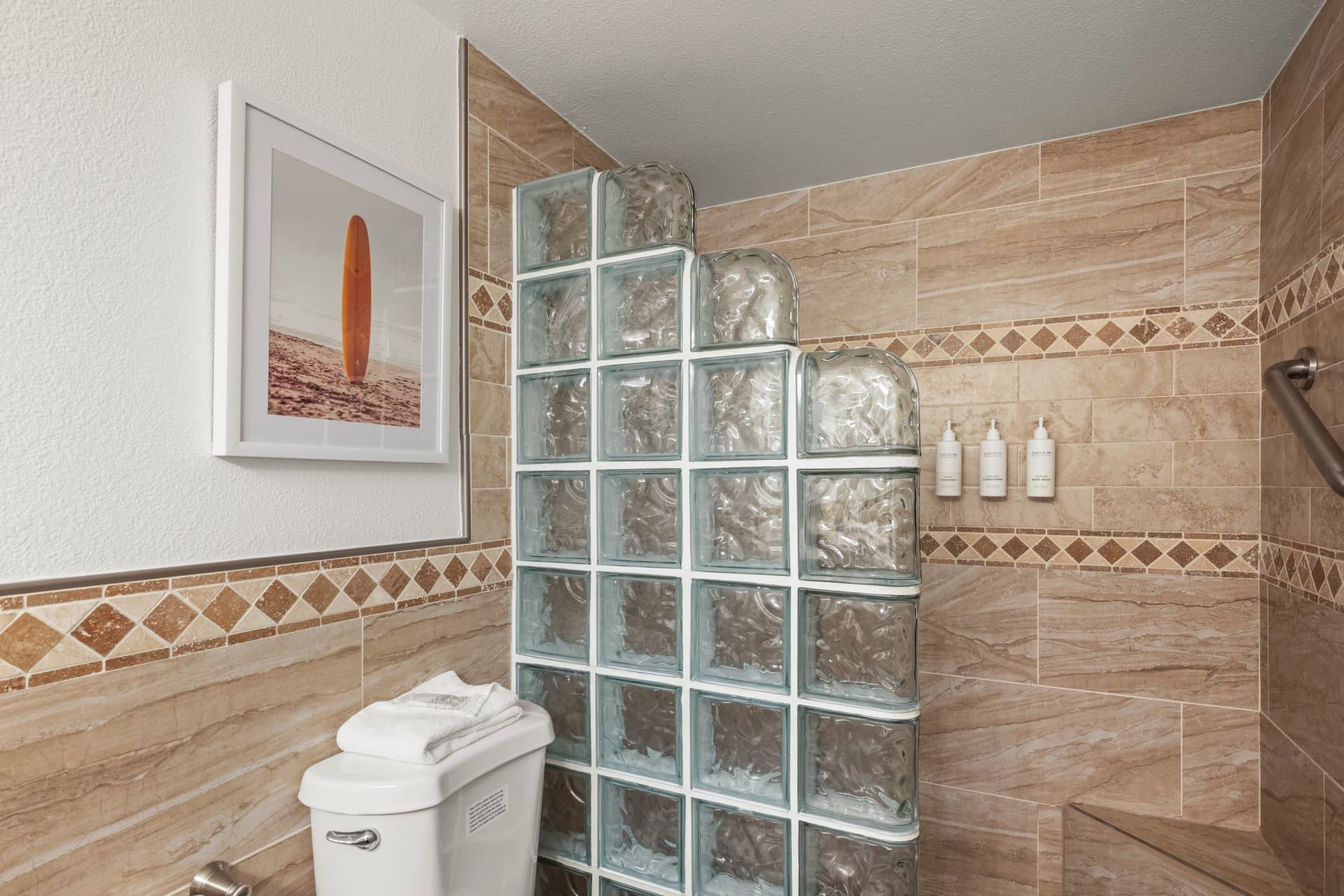 A bathroom with a glass shower enclosure, a toilet, and a framed picture on the wall.