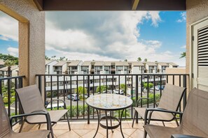 A balcony with two chairs and a table, overlooking a row of apartment buildings and a parking area.