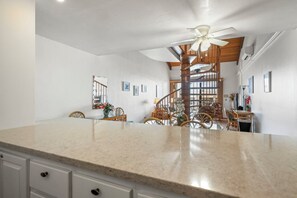 A kitchen with a granite countertop, wooden chairs, and a ceiling fan.