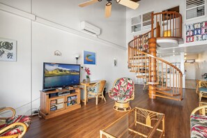 A spacious living area with a wooden staircase, a flat-screen TV, and a variety of seating options.