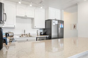A modern kitchen with white cabinetry, stainless steel appliances, and a marble countertop.