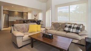 A modern living room with two sofas, a coffee table, and a kitchen in the background. - Northview 2 - Modern 2BR Townhouse l Lake View l Central Location l Spa Bath l WiFi (JINDABYNE)
