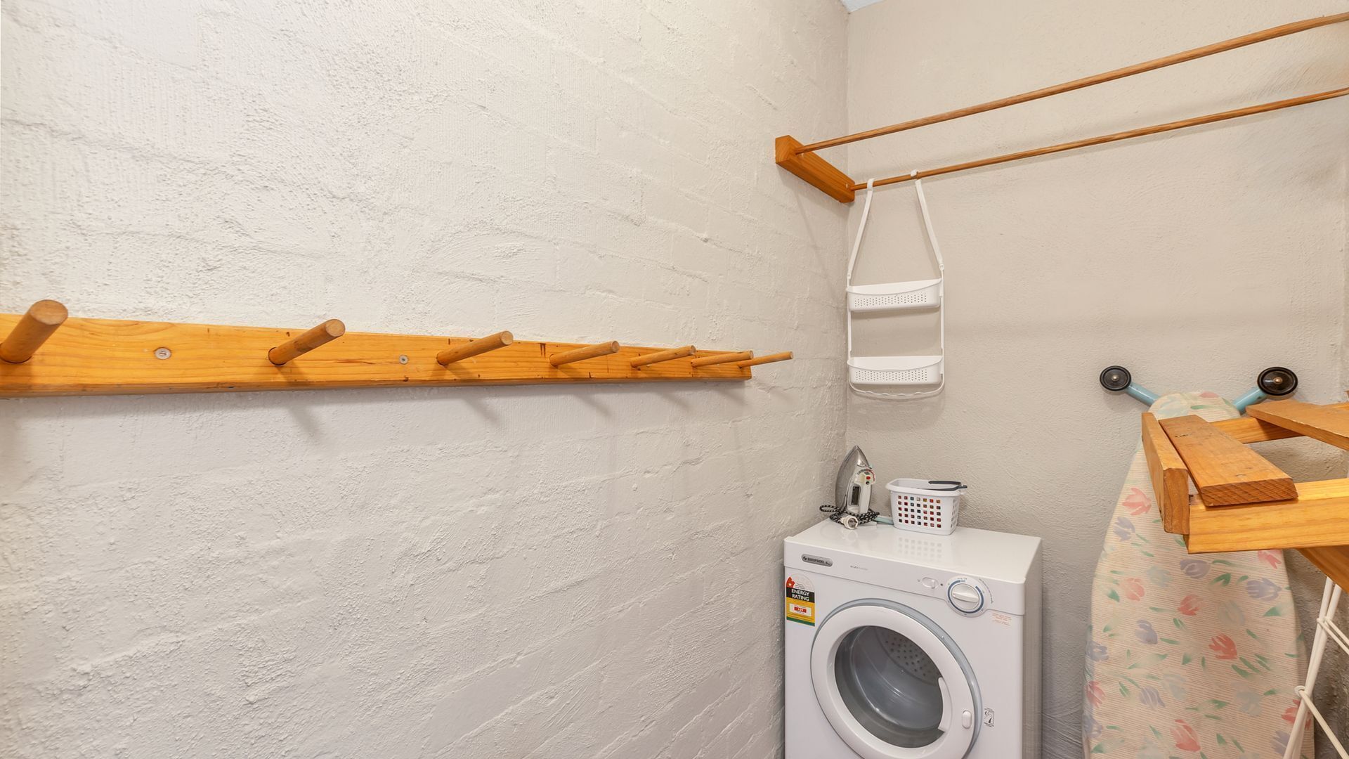Un área de lavandería con lavadora, tendedero y cesta para colgar ropa.
