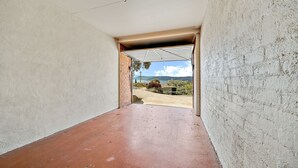 A narrow hallway with a concrete floor leading to an open area with a view of a landscape and a body of water.