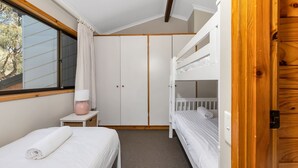 A bedroom with a bunk bed, a single bed, a bedside table with a lamp, and a wardrobe.