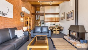 A cozy living room with a fireplace, a sofa, a coffee table, and a kitchen in the background.
