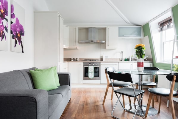 A modern kitchen with white cabinets, a stainless steel range hood, and a dining area with a glass table and chairs.