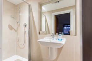 Ein Badezimmer mit Duschkabine aus Glas, einem Waschbecken mit Spiegel und einem Fenster.