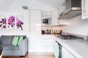 A modern kitchen with white cabinets, a microwave, a stove, and a green kettle.