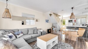 A modern living room with a grey sofa, a white coffee table, and a fireplace. There is a kitchen area with a dining table and chairs.